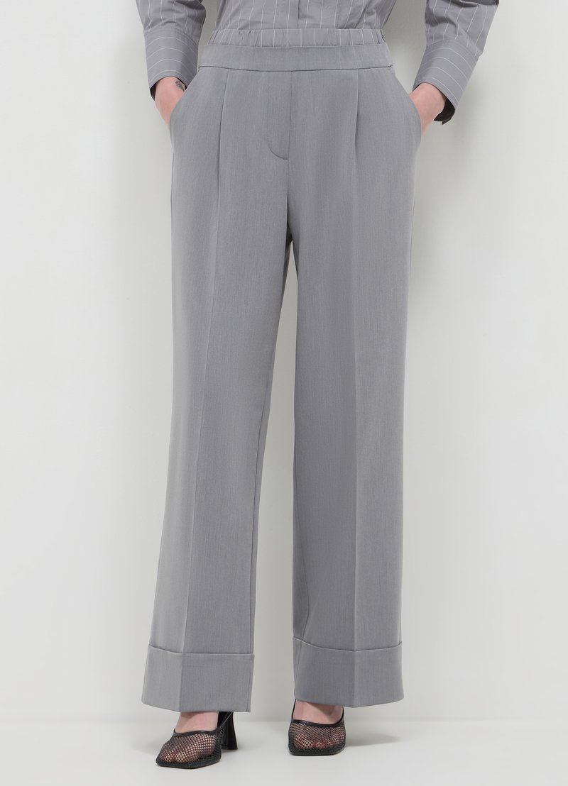 Pantalons gris à jambes larges avec une texture lisse, dotés de poches latérales et d'un ourlet à revers. Portés avec des chaussures à talons hauts en mesh noires.