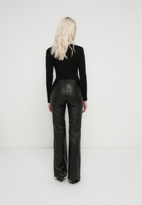 Haut noir ajusté à manches longues, associé à un pantalon en cuir noir taille haute, évasé, présentant une texture lisse et des détails de couture minimalistes.