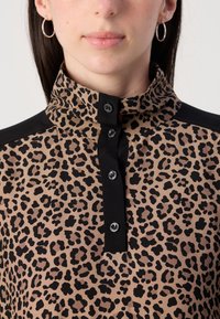 Leopardenmuster-Bluse mit hohem Kragen, schwarzem Knopfleiste und kontrastierenden schwarzen Akzenten an den Schultern, aus einem weichen Stoff gefertigt.