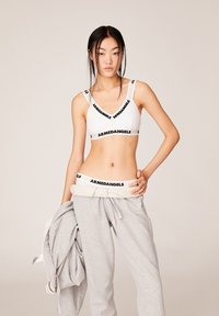 Witte bralette en hoog getailleerde grijze sweatpants, met een zwart "ARMEDANGELS" logo op de elastische banden, gladde textuur, minimalistisch ontwerp.