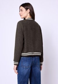Olivenfarbener, cropped Pullover mit gerippten, weiß gestreiften Bündchen und Saum, gefertigt aus weichem Strickmaterial. Kombiniert mit hoch taillierten blauen Jeans.
