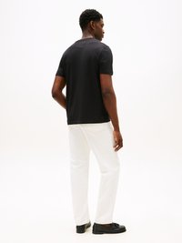 Black short-sleeve t-shirt, white straight-leg jeans, and black loafers. Smooth fabric, simple design, no patterns or graphics visible.