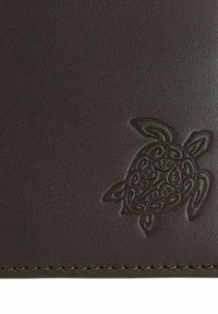 Surface en cuir marron foncé avec un bord surpiqué et un motif gaufré de tortue de mer style tribal dans le coin inférieur droit.