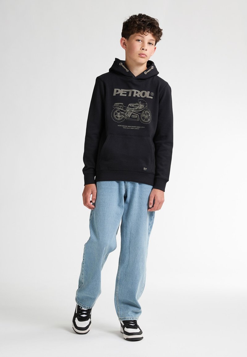 Felpa nera con cappuccio e grafica di motocicletta grigia, abbinata a jeans blu chiaro e sneakers nere e bianche. Design minimalista.