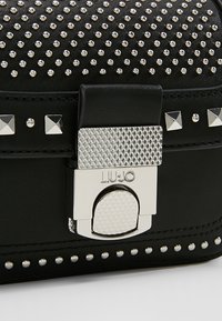 Svart läderväska med silvernitar och ett strukturerat silverlås graverat med "LIU JO"-logotyp.