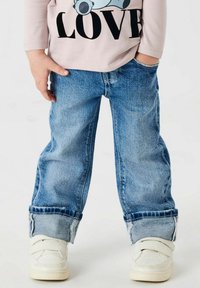 Jeans de mezclilla de color azul claro con un corte relajado y puños doblados, combinados con zapatillas blancas con correas de Velcro.
