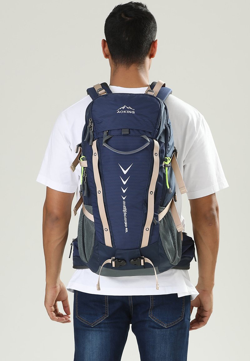 Zaino blu navy con spalline beige, caratterizzato da un design testurizzato, molteplici scomparti, tasche laterali in rete e fibbie regolabili.