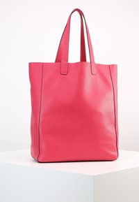 Sac fourre-tout en cuir rose avec une finition texturée, deux poignées plates, ouverture en haut et surpiqûres noires sur les côtés. Forme carrée.