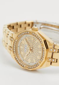 Gold metal wristwatch with octagonal case, crystal accents on bezel, and a sparkling dial. Stainless steel bracelet links, luminous hands.