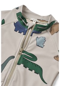 Rash guard couleur crème avec des motifs de dinosaures multicolores. Il possède une fermeture éclair à l'avant et un col haut pour plus de protection.