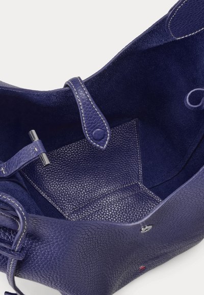 Detailní záběr prázdné otevřené tmavě modré kožené kabelky ukazující texturovaný vnitřek s popruhem a stříbrnými zapínacími detaily.