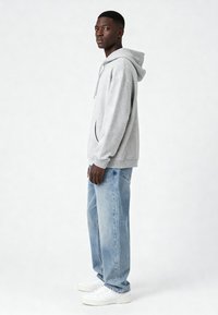 Sivá mikina s kapucňou a predným vreckom, skombinovaná so svetlomodrými džínami a bielymi teniskami. Pohodlný strih, mäkká textúra a rebrované manžety.