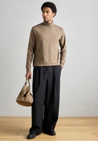 Pruun pikkade varrukatega kõrgekaelus triiksärk peene logoga, mida on kombineeritud lahtiste mustade pükstega ja pruuni nahast kotiga. Mustad massiivsed kingad.