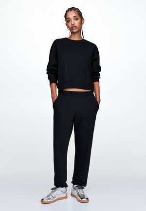 Zwart cropped sweatshirt met lange mouwen, gecombineerd met zwarte joggers met een elastische tailleband. Zilveren sneakers met een textuurdesign.