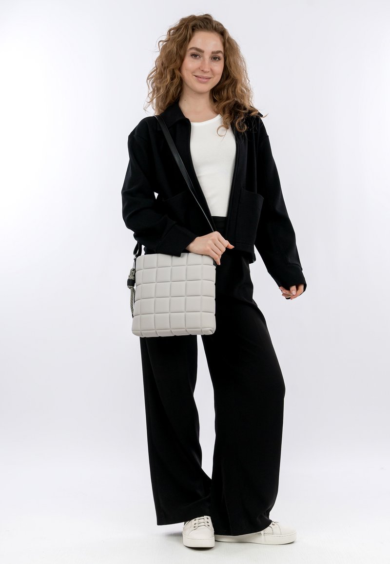 Giacca nera corta sopra una maglietta bianca, abbinata a pantaloni neri a gamba larga e sneakers bianche. La borsa è grigia, con una texture a quadri trapuntati.