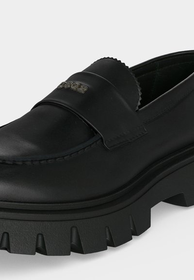 Mocassin en cuir noir avec semelle épaisse à rainures et logo métallique "DSQUARED2" sur la bride en haut.