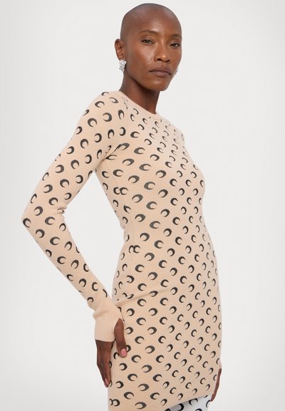 Vestido de punto de manga larga en beige con un patrón de luna creciente negra, silueta ajustada y puños acanalados. Textura suave y cuello redondo.
