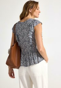 Bluse med blomsterprint i marineblå farve med korte, flæseærmer og elastisk talje. Sammen med off-white, løstsiddende bukser og en brun tote bag.