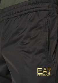Pantaloni sportivi neri realizzati in tessuto leggero. Presentano una fascia elastica in vita, una tasca laterale e il logo dorato EA7 Emporio Armani.