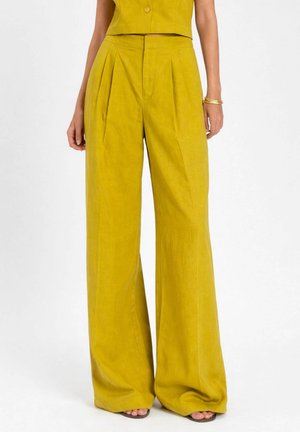 Donna che indossa pantaloni a vita alta, gamba larga color giallo senape con pieghe, abbinati a top corto senza maniche coordinato e sandali.