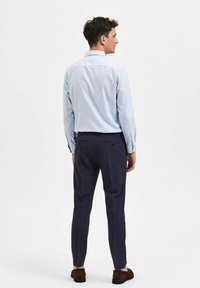 Lys blåstripet skjorte med lange ermer, kombinert med mørkeblå slim-fit bukser og brune suedestøvler. Utsikt fra baksiden.