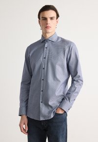 Camicia abbottonata a quadri blu e bianchi, con maniche lunghe, colletto a punta e bottoni blu. Il tessuto sembra liscio e leggero.