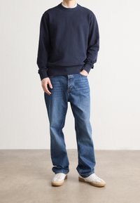 Námořnická mikina s kulatým výstřihem, kombinovaná s světle modrými džínami a bílými teniskami s hnědými podrážkami. Ležérní střih, minimální designové detaily.