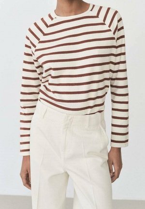 Personne portant une chemise blanche à manches longues avec des rayures horizontales marron, rentrée dans un pantalon taille haute écru.
