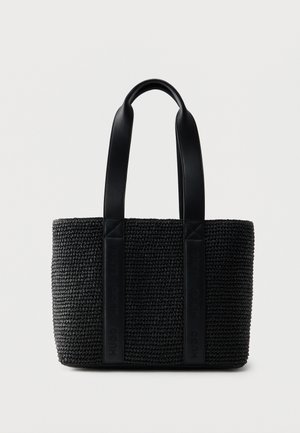 Bolsa tote tejida negra con dos asas de cuero anchas y sutil marca en relieve en las correas de las asas, sobre un fondo blanco liso.