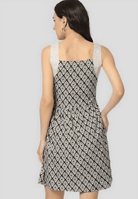 Vestido en blanco y negro con un patrón de diamantes, diseño sin mangas y cintura ceñida. El material parece ligero y tiene una textura suave.