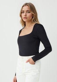 Body nero a maniche lunghe con scollatura quadrata, realizzato in tessuto morbido, abbinato a pantaloni bianchi a vita alta.