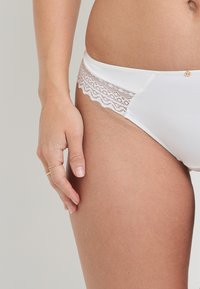 Culotte blanche à dentelle, en tissu doux, avec des bords en dentelle festonnée et un petit bouton décoratif sur la taille.