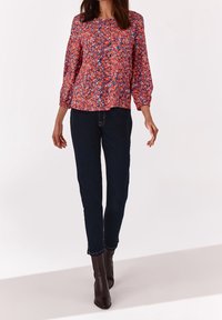 Blomsterprintet bluse i pink, orange og blå med trekvart ærmer; parret med mørk denim jeans og brune ankler støvler.