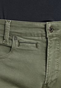 Gröna byxor i bomullsblandning med dragkedja, knappstängning och femfickorsdesign. Har en unik ficka med klaff på framsidan.