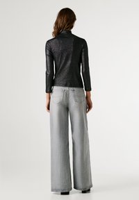 Μαύρος, μεταλλικός τοπ με μακριά μανίκια και ψηλό γιακά, συνδυασμένος με ανάλαφρα γκρι τζιν με άνετη εφαρμογή και πίσω τσέπες. Λείος υφής, ελάχιστη λεπτομέρεια.