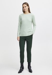 Light green knit sweater with a round neckline and raglan sleeves, paired with dark green slim trousers and black ankle boots.