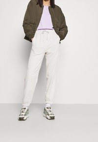 Olivová bomber bunda, levandulové tričko, světle šedé tepláky s elastickými manžetami a zeleně akcentované tenisky s tkaničkami a detailem na podrážce.