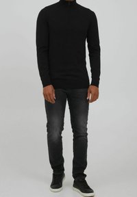 Musta vetoketjullinen neule, joka on muotoiltu istuvaksi, yhdistetty tummanharmaisiin farkkuihin ja mustiin lenkkareihin. Silkkinen rakenne minimalistisella tyyliasennolla.