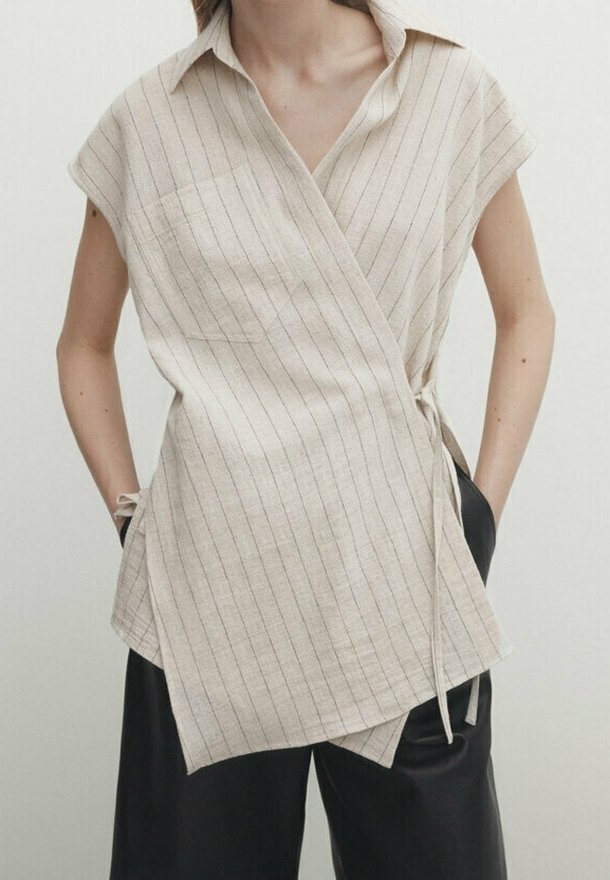 Top senza maniche a righe beige realizzato in un tessuto leggero, con colletto e dettagli con fiocco laterale. Presenta una tasca sul petto e una vestibilità ampia.