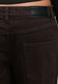 Καφέ παντελόνια από denim με ομαλή υφή, δερμάτινη πίσω ετικέτα με λογότυπο και μια πί σω τσέπη με αντίθετη ραφή.