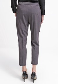 Pantalones grises ajustados con una textura suave, cinturilla elástica y un bolsillo trasero, combinados con zapatos de tacón negro.