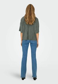 Grå plisseret top med løs pasform, korte ærmer og buet kant, parret med lyseblå flare jeans og sorte hæl støvler.