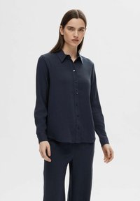 Navy blue long-sleeve shirt made of textured fabric, featuring a button-down front and classic collar, worn with matching pants.
