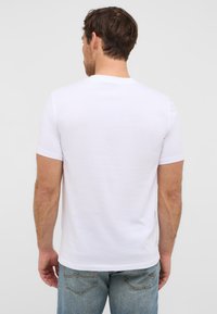 Biała koszulka z krótkim rękawem, okrągły dekolt, dopasowany krój, gładka bawełniana tkanina, klasyczny widok z tyłu, zestawiona z jasnoniebieskimi dżinsami.