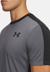Camiseta atlética gris con detalles negros, de manga corta, cuello redondo, textura suave, con un logo negro en el pecho.