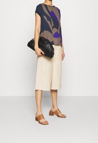 Volnější top s námořnickou a hnědou vzorovanou texturou doplněný béžovými culotami. Černá texturovaná psaníčko a hnědé sandály na podpatku.