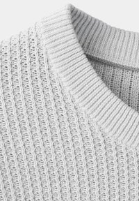 Gros plan d'un pull tricoté gris clair avec une texture côtelée verticale et un col rond épais et plié.