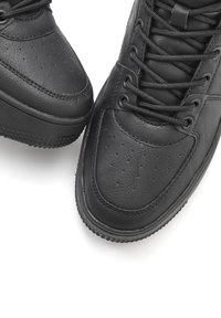 Schwarze Ledersneaker mit strukturierter Oberfläche, durchlöchtem Zehenbereich, dickem Gummisohle und schwarzen Schnürsenkeln. Schlichtes Design ohne Verzierungen.