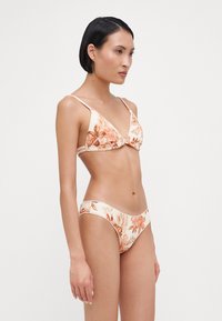 Kvetinový bikiny set z jemnej béžovej látky, ktorý obsahuje trojuholníkový vrch s tenkými popruhmi a zodpovedajúce spodné diely s nízkym pásom ozdobené oranžovými a hnedými kvetinovými vzormi.