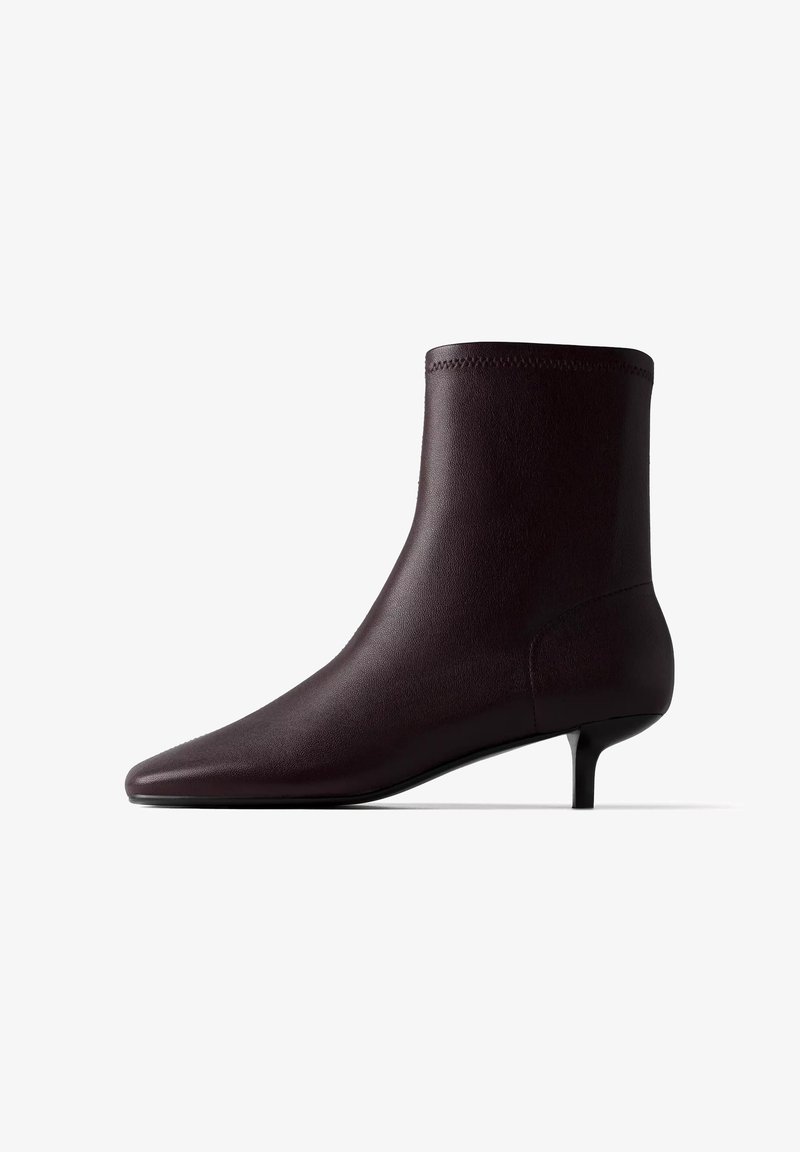 Bottine en cuir marron foncé avec bout pointu et petit talon kitten sur fond blanc.